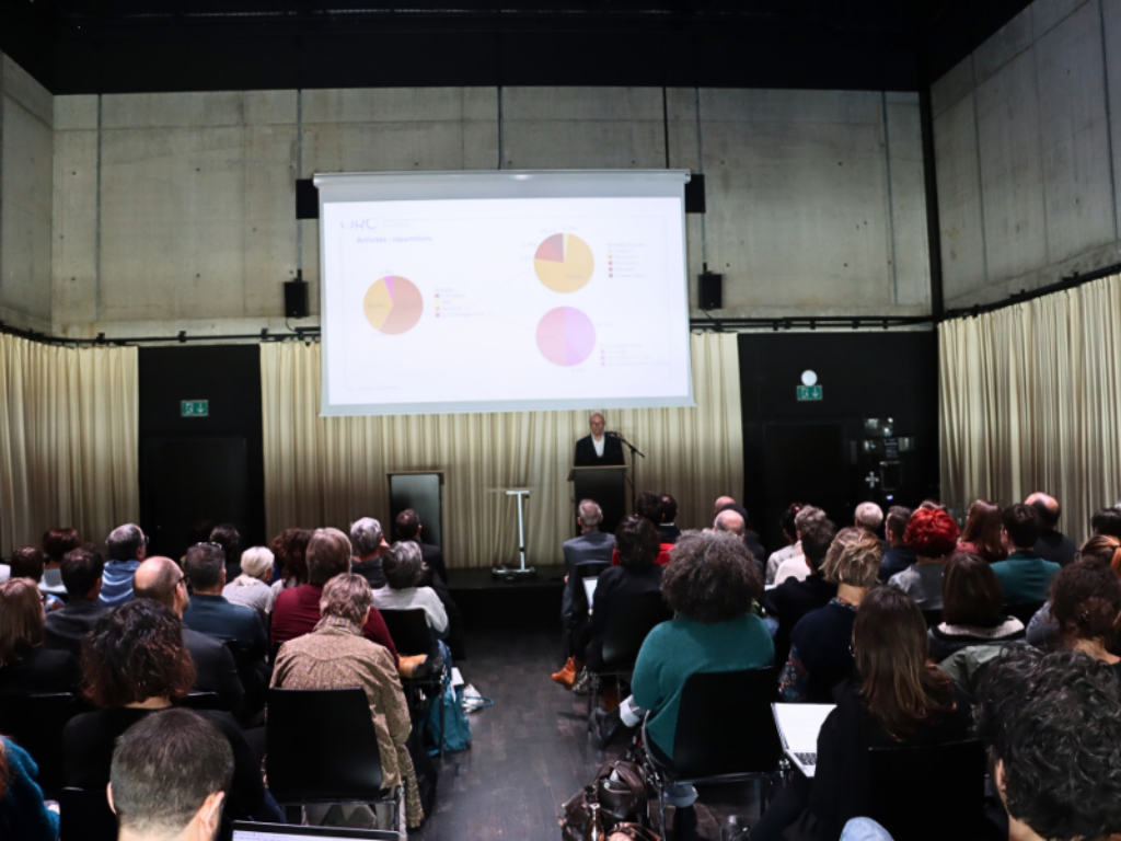 Un conférencier présente une slide avec des camemberts, devant un public assis.